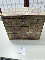 Front view of antique wooden jewelry box showing brass hardware and multiple drawers closed.