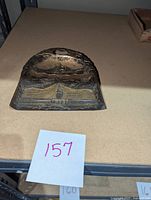 Frontal photo of decorative crumb butler placed on flat surface with number 157 marked in front.