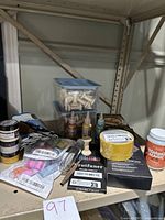 Various art and craft supplies spread on shelving including paint brushes, jars, metallic pencils, chalk paste, and wooden figures.
