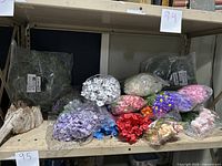 Shelf with various bunches of artificial flowers in multiple colors, with some flowers and greenery in plastic bags.