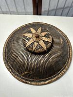 Top view of circular woven bamboo, straw, and rattan hat showing 8 pointed star design on raised center dome.
