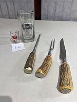 Full set including beer glass, cocktail jigger, and three cutlery tools with antler handles laid on table with a lot number card.