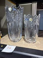 Two Bohemia Crystalex clear crystal vases, one tall and one short, showing cut leaf-like patterns and jagged tops with original stickers