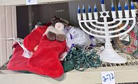 Photo shows Chanukah menorah light with blue flames, several red Christmas stockings with plush animal decorations, and a bundle of green Christmas string lights.