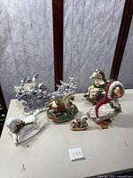 All holiday figurines including four rocking horses, Christmas duck, Santa's sleigh with reindeer arranged on table.
