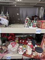 View of snowmen figurines, ceramic vase, gift boxes, tinsel decorations, and candy canes on a shelf