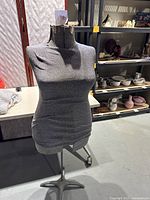 Full view of grey fabric dress form mannequin on metal wheeled stand.
