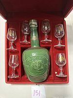 Red velvet-lined box containing a decorative green ceramic Sauza tequila bottle and six shot glasses arranged around it.