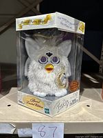 Front view of unopened Special Limited Edition Angel Furby in clear protective packaging showing white fur, angel wings, purple eyes, and yellow beak.