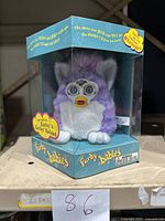 Purple and white Furby Baby toy housed inside original clear plastic display box with blue and yellow branding and descriptive text.