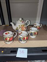 Teapot and four tea cups arranged on a table, showing detailed fruit artwork on each piece.