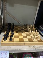 Full view of wooden chess board with black and white chess pieces set up on the board, showing felt-lined inner storage.