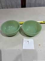 Two jadeite green bowls side by side with tape measure showing size about 4.5 inches diameter