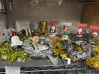 Shelf display showing assorted Christmas garlands, a soft fabric angel tree skirt, a lit angel tree topper, and four boxed solar dancing holiday character toys including penguin, elf, and Santa.