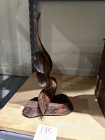 Side angle photo of the dark wood sculpture showing the spherical and curved abstract fluid shape on a flat base