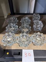 Seven Indiana Glass starburst style candle holders and two clear glass cube candlestick holders arranged on a surface