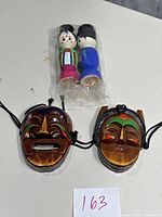 Photo showing both wooden Korean masks with expressive painted faces alongside two traditional Korean wooden dolls in plastic wrap.
