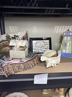 Overview photo showing all items in the nautical decor lot arranged on a shelf: stained glass lighthouse, ceramic shell dish, potpourri box, vintage pins box, colorful blanket with lighthouse theme, and framed Rocky Point print.
