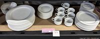 Full set of stacked plates, cups, and saucers displayed on shelf showing counts and overall condition.