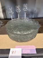 Stack of ten clear glass plates with embossed rose and leaf floral patterns, scalloped edges.