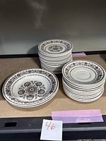 Stack of dinnerware plates and bowls showing brown floral pattern on white ceramic.