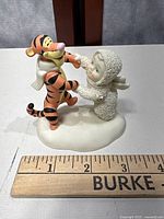 Close-up photo of Snowbabies figurine holding hands with Tigger character for size reference with ruler