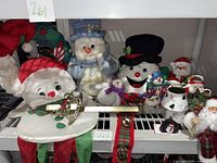 Shelved display of various plush snowmen, Santa soft decoration, ceramic and holiday items arranged together