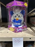 Close view of Special Millennium Edition blue and grey Furby inside hexagonal packaging with phrases and branding visible on box.