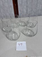 Six clear stemless wine glasses arranged together on a white surface.