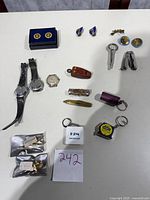 Full lot overview showing military pins, cufflinks, watches, pocket cutters, and keychains on a table.