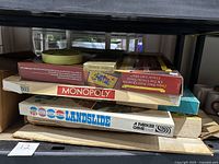 Stack of vintage board games including Monopoly, Landslide, Risk, and others shown on shelf.