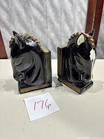 Two black and beige ceramic horse head bookends shown side by side, one with visible chip on horse's head and crazing on surfaces