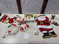 Photo showing a collection of vintage Christmas decorations including multiple Santa figures, a NOEL hanging sign, and packaged vintage lit Santa head and sleigh light.