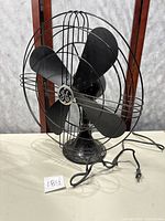 Full view of vintage General Electric fan showing 4 blades, protective wire cage, base, and attached cord.