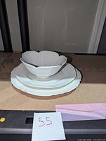 Three white porcelain items stacked: a lotus-shaped bowl on top, a luncheon plate in the middle, and a dinner plate below, all with scalloped edges.