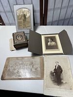 Vintage leather photo album with visible portrait inset on cover, surrounded by loose vintage photographs including studio portraits and group photo on a white table