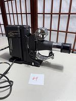 Side angle of the vintage projector showing lens and carrying handle with attached power cord.