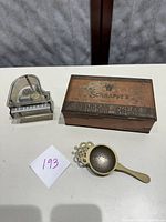 Photo showing all three items together: vintage Schraffts Crimson Chest candy tin, grand piano music box, and brass tea strainer on white surface with a paper label '193'