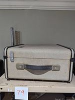 Front of textured off-white carrying case with black trim and handle, showing clasp and handle detail
