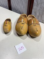 Three wooden clogs displayed on a white surface. Two larger adult-style clogs and one smaller child-size clog, painted yellow with black decorative patterns on top. The child clog shows some wear on the toe.