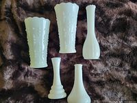 Group photo showing all five white milk glass vases arranged on a dark textured background, displaying size and shape differences.