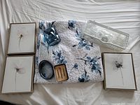 Three framed flower prints, white and black, plus blue glass container and dishes, grey soap dish, and folded floral shower curtain.