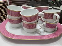 Close up image of stacked cups on a platter showing raspberry pink geometric pattern with gold rim
