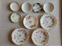 Top-down photo showing arrangement of 9 butter pats and small plates on fabric surface with floral and decorative patterns.