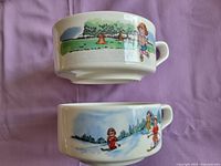 Side views of two ceramic soup mugs/bowls featuring Campbell Soup Kids scenes, one with kids in a park and the other with kids skiing.