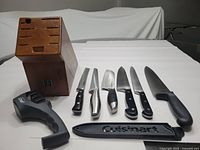 Wooden knife block, 7 knives of various brands and styles, black Cuisinart sheath, steel fork, and black Master Chef sharpener on white background.