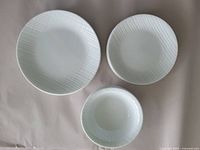 Top view of individual dinner plate, luncheon plate, and soup bowl showing white linen weave pattern.