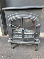 Front view of electric heater resembling a wood stove with glass doors and metal latch