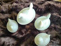 Set of four white milk glass hens on nests displayed on dark fabric background to show size and shape differences.