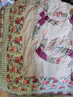 Folded quilt showing floral and plaid fabric in border and double wedding ring patchwork with varied fabric colors including pink, green, red and purple.